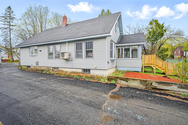 view of front of house with a shingled roof, a sunroom, a chimney, and stairway