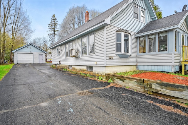 view of property exterior with a garage, a chimney, a sunroom, an outdoor structure, and driveway