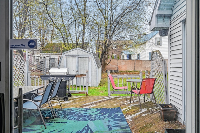 wooden terrace featuring a shed, fence, an outbuilding, and a grill