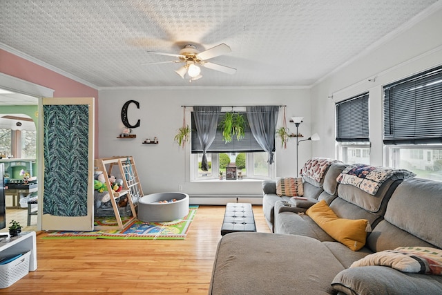 living room featuring baseboard heating, wood finished floors, ornamental molding, a ceiling fan, and a textured ceiling