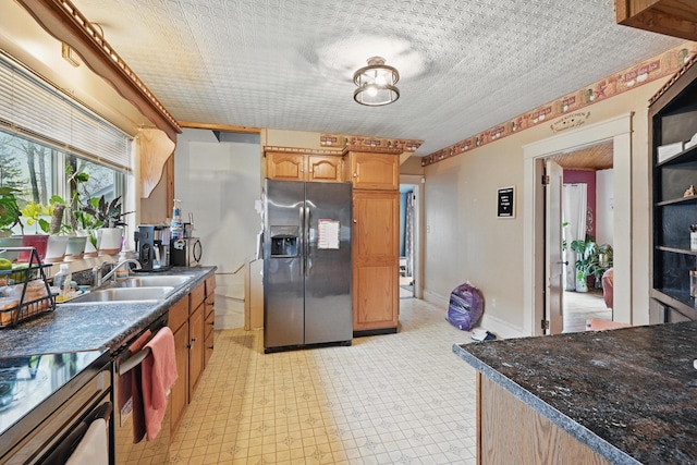 kitchen with appliances with stainless steel finishes, a sink, dark countertops, light floors, and a textured ceiling