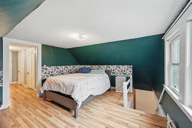 bedroom featuring a textured ceiling, wood finished floors, baseboard heating, lofted ceiling, and baseboards
