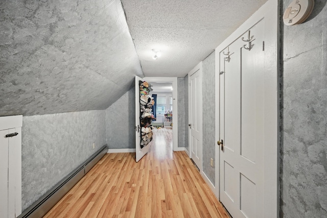 corridor with baseboard heating, wood finished floors, a textured ceiling, lofted ceiling, and baseboards