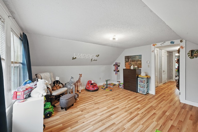 recreation room with light wood-style flooring, lofted ceiling, baseboards, and a textured ceiling