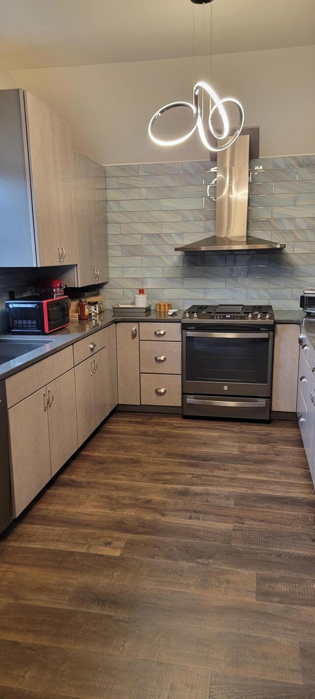 kitchen featuring stainless steel gas stove, wall chimney range hood, dark countertops, and dark wood-style flooring
