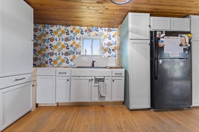 kitchen with freestanding refrigerator, a sink, wood ceiling, white cabinetry, and light wood-style flooring