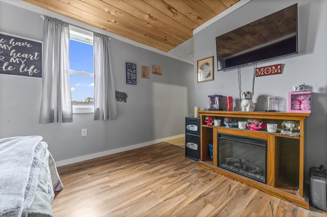 bedroom with wood ceiling, wood finished floors, baseboards, and a glass covered fireplace