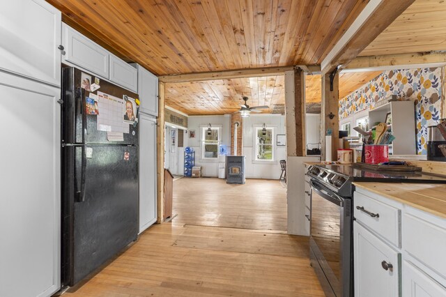 kitchen with black appliances, a wood stove, white cabinetry, wood ceiling, and light wood-style flooring