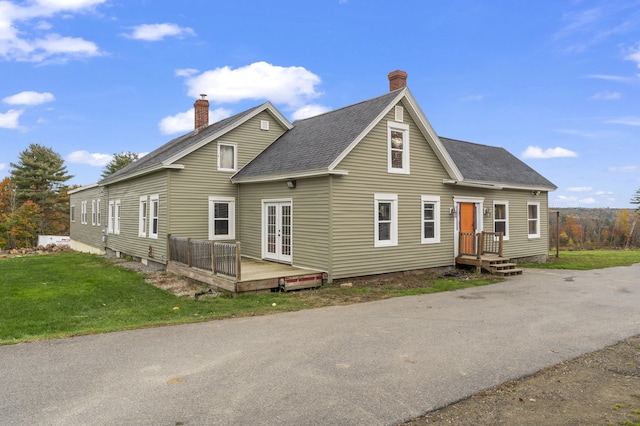 view of front of property with a shingled roof, a front yard, french doors, a deck, and a chimney