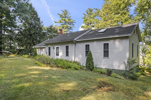 view of side of property featuring a chimney, a lawn, and roof with shingles