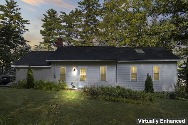 back of property at dusk featuring a chimney and a lawn