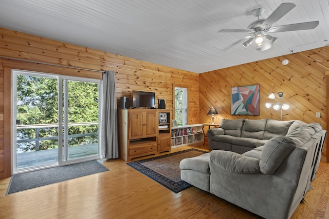 living room with light wood-style floors, ceiling fan, and wooden walls