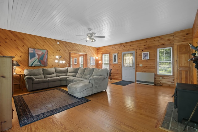 living room featuring a ceiling fan, a wood stove, wood walls, and light wood-type flooring
