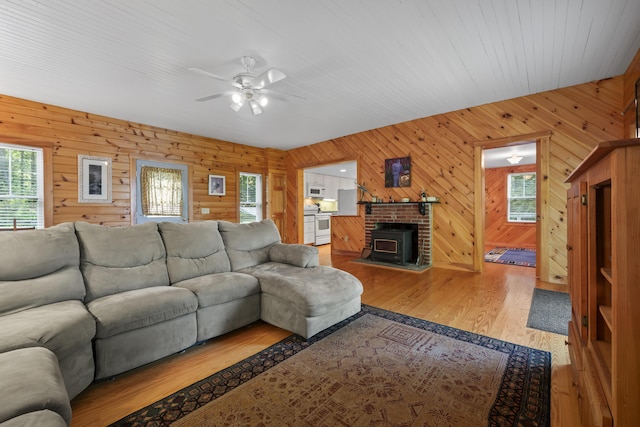 living room with ceiling fan, wood finished floors, wood walls, and a wood stove