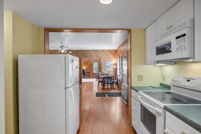 kitchen with white appliances, wooden walls, white cabinets, light wood-style floors, and an accent wall
