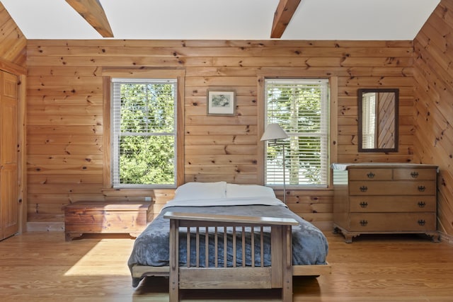 bedroom featuring beam ceiling, light wood-style flooring, and wood walls