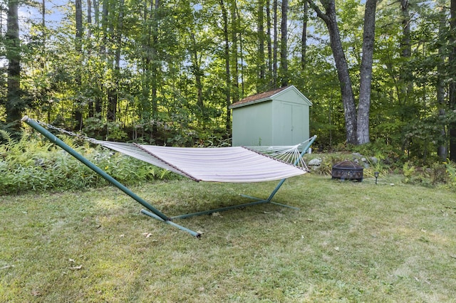 view of grassy yard with an outdoor fire pit, a storage unit, and an outdoor structure