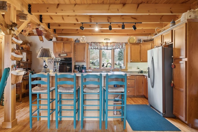 237 River Rd, Avon, ME 04966 - kitchen with stainless steel fridge with ice dispenser, light wood finished floors, brown cabinets, a breakfast bar area, and beamed ceiling