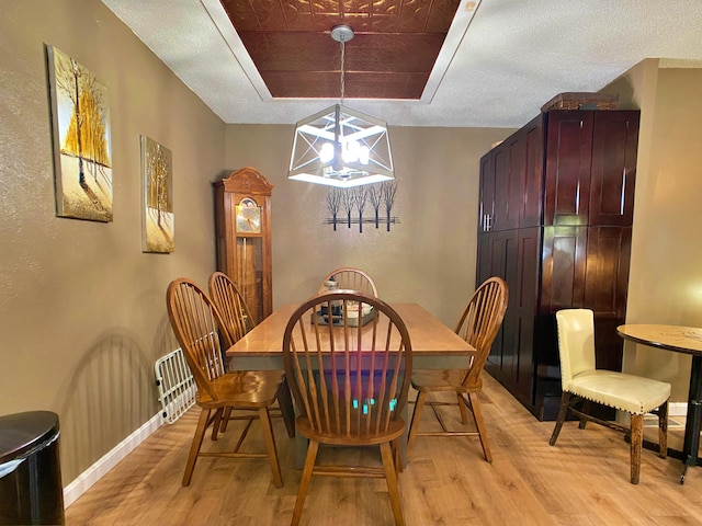 dining area with light wood-style floors, a textured wall, a chandelier, baseboards, and a textured ceiling