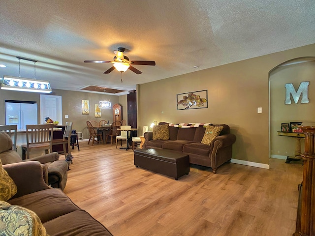 living room featuring a textured ceiling, a ceiling fan, light wood-type flooring, arched walkways, and baseboards