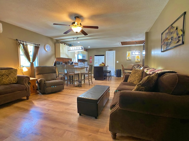 living area featuring a ceiling fan, a textured ceiling, healthy amount of natural light, and light wood-style flooring