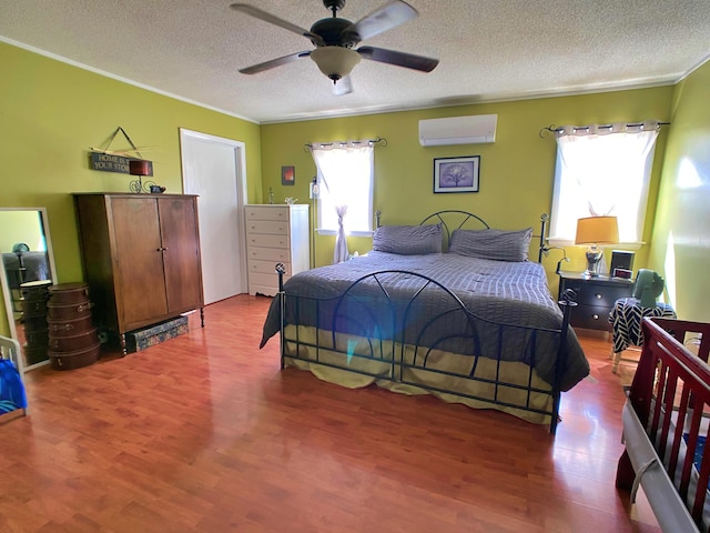 bedroom with a wall mounted AC, crown molding, a textured ceiling, wood finished floors, and ceiling fan