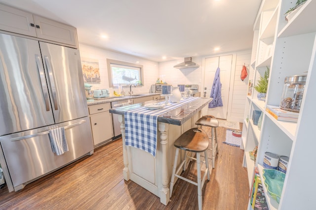 kitchen with stainless steel appliances, a sink, wood finished floors, a center island, and a kitchen bar
