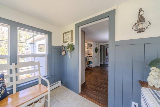 doorway to outside with wood finished floors, wainscoting, a decorative wall, ornamental molding, and a baseboard radiator