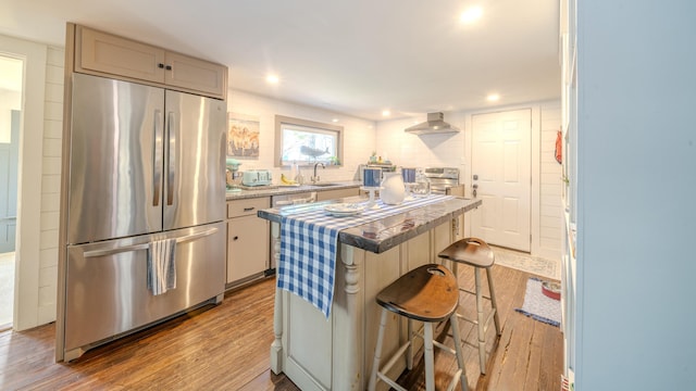 kitchen with appliances with stainless steel finishes, wood finished floors, wall chimney range hood, a kitchen island, and a sink