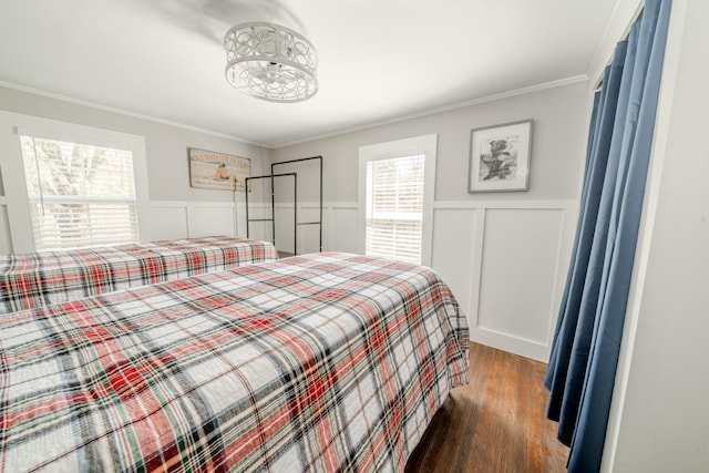 bedroom featuring wood finished floors, a wainscoted wall, multiple windows, ornamental molding, and a decorative wall