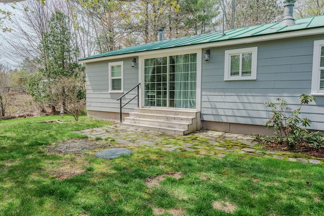 rear view of property with entry steps, a lawn, and metal roof