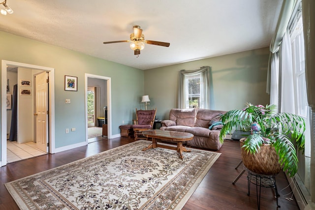 living area with ceiling fan, wood finished floors, a baseboard heating unit, and baseboards