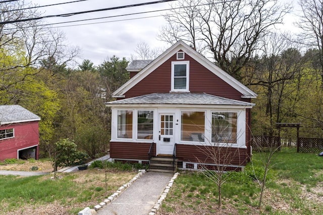 bungalow-style home featuring a shingled roof, entry steps, a view of trees, and fence