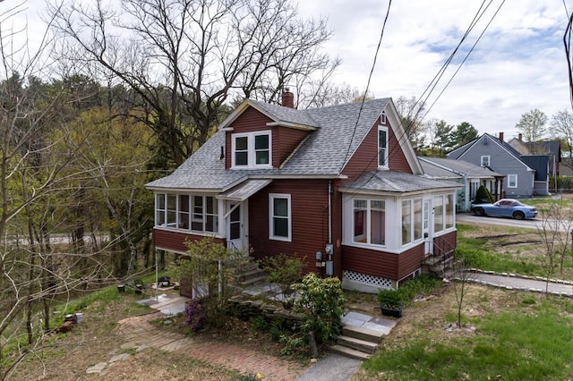 view of front of home featuring a sunroom, roof with shingles, a chimney, and entry steps