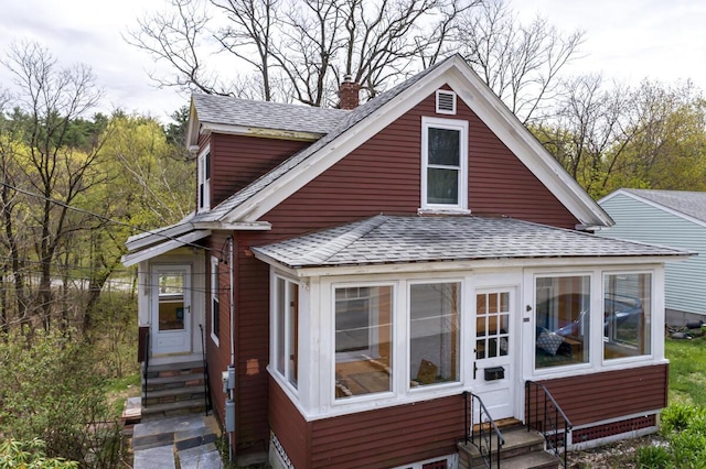 bungalow with entry steps, roof with shingles, a chimney, and a sunroom
