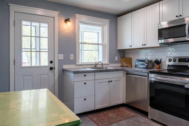 kitchen with stainless steel appliances, a sink, backsplash, white cabinetry, and dark wood finished floors