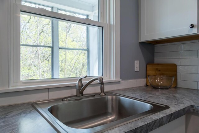 kitchen view of a sink, white cabinets, and backsplash