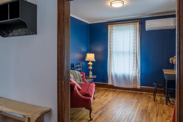 sitting room with a wall mounted air conditioner, hardwood / wood-style floors, ornamental molding, and baseboards
