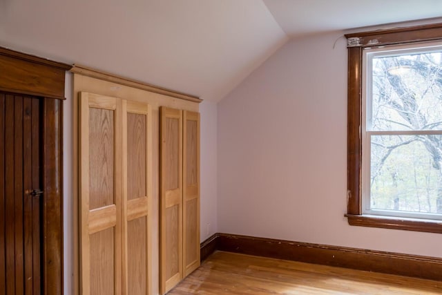 unfurnished bedroom with vaulted ceiling, light wood-style floors, and baseboards