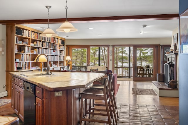 kitchen featuring tile counters, dishwasher, a sink, wood finished floors, and a breakfast bar