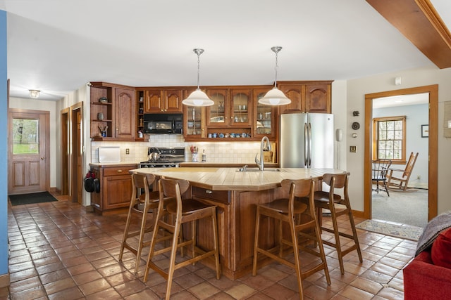 kitchen featuring black microwave, open shelves, freestanding refrigerator, light countertops, and a sink
