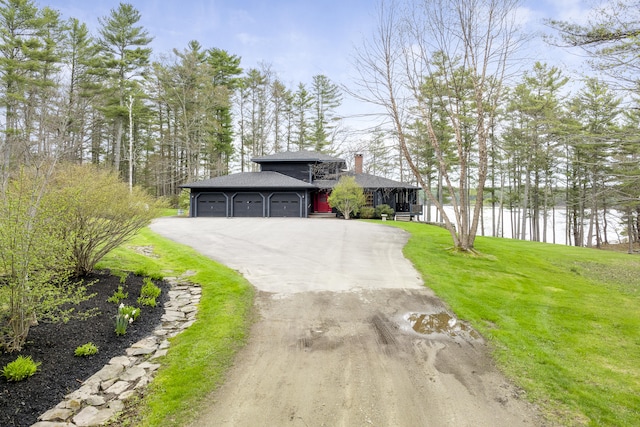 view of front of property featuring an attached garage, a shingled roof, a front lawn, a chimney, and asphalt driveway