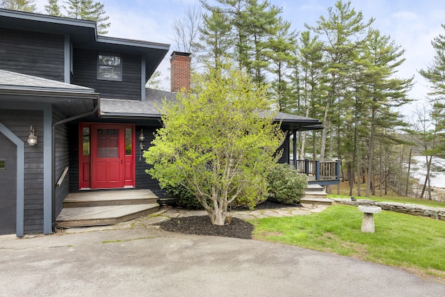 view of exterior entry featuring a chimney, roof with shingles, and a lawn