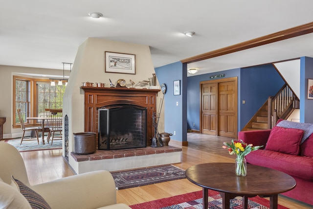 living room featuring wood finished floors, a fireplace with raised hearth, stairs, a chandelier, and baseboards