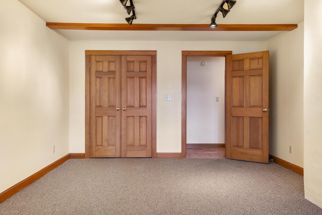 unfurnished bedroom with carpet flooring, track lighting, and baseboards