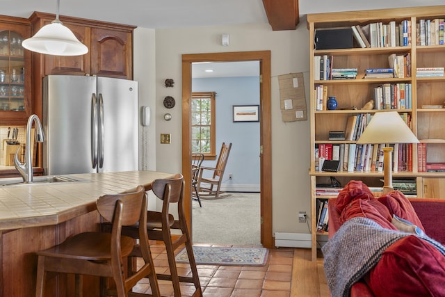 kitchen featuring freestanding refrigerator, a sink, tile counters, glass insert cabinets, and hanging light fixtures