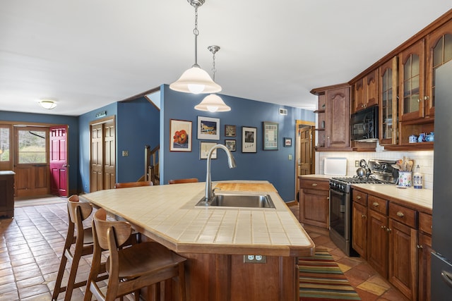 kitchen with gas stove, a sink, black microwave, tile countertops, and backsplash