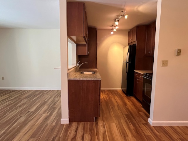 kitchen featuring a sink, black appliances, dark wood-style floors, and baseboards