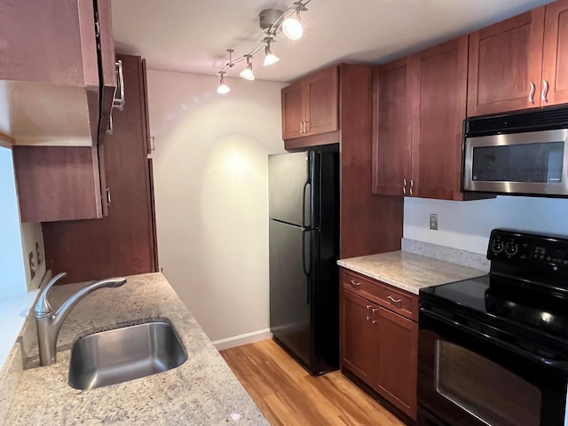 kitchen featuring black appliances, a sink, light wood-style flooring, and light stone counters