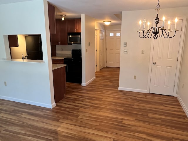 kitchen with electric range, stainless steel microwave, wood finished floors, a chandelier, and baseboards